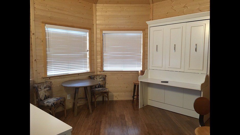 Cozy wooden room with two windows, a small round table, and white built-in cabinets on the right.