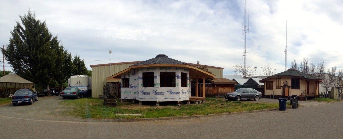 Small roadside building with a white banner, parked cars, and trees under a cloudy sky