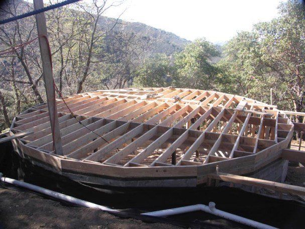 Wooden roof frame under construction in a wooded hillside area