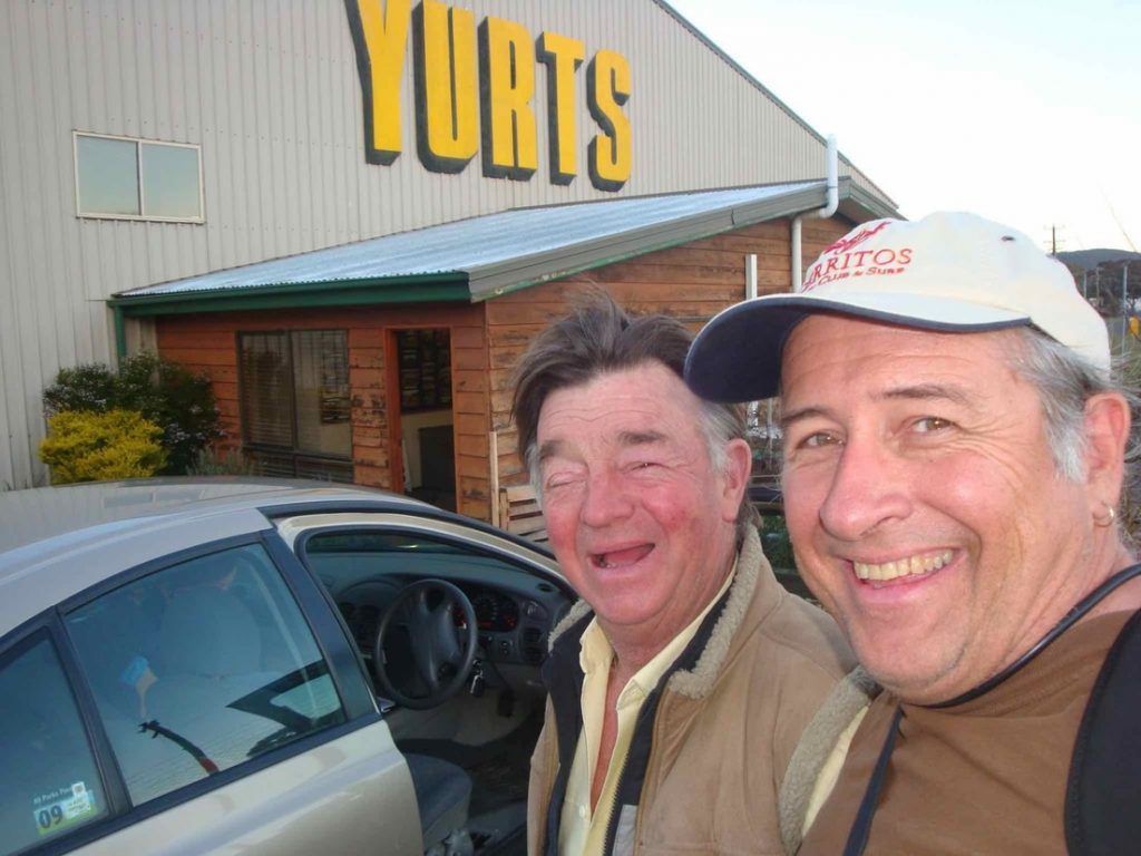 Two smiling people posing beside a car in front of a building labeled “Yurts”