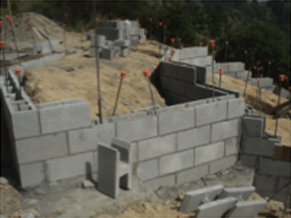 Partially built cinder block wall at a construction site with scattered materials and dirt ground