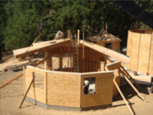 Wooden house frame under construction with plywood walls and scaffolding outdoors