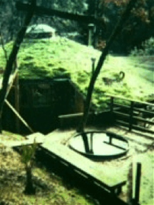 Old rural well with a circular cover and wooden fence on a grassy hillside