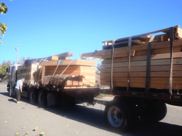 Flatbed truck loaded with wooden planks driving on a sunny road under a clear blue sky