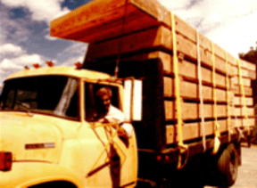 Yellow flatbed truck loaded with stacked wooden planks on a road