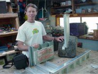 Person in a workshop beside a green-topped machine and a large metal block on a workbench.