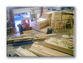 Woodworking workshop with stacked lumber, tools, and a worker near the open doorway
