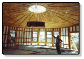 Wide circular room with wooden dome ceiling and large windows; a person stands near the right side.