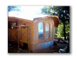 Partially built small wooden house with arched windows and scaffolding in a sunny yard