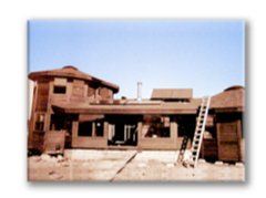 Desert-style house with wooden upper level and a ladder leaning against it under a blue sky