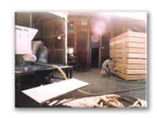 Warehouse interior with stacked wooden pallets and a worker bending near equipment.