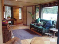 Cozy living room with sofa, rug, wooden walls, and large window overlooking greenery