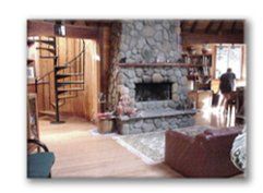 Rustic living room with stone fireplace, spiral staircase, and wooden beams