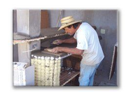 Man in a straw hat bending over an outdoor grill or oven, working with food or embers
