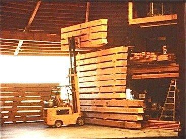 Forklift lifting stacked wooden pallets in a warehouse with a ladder nearby