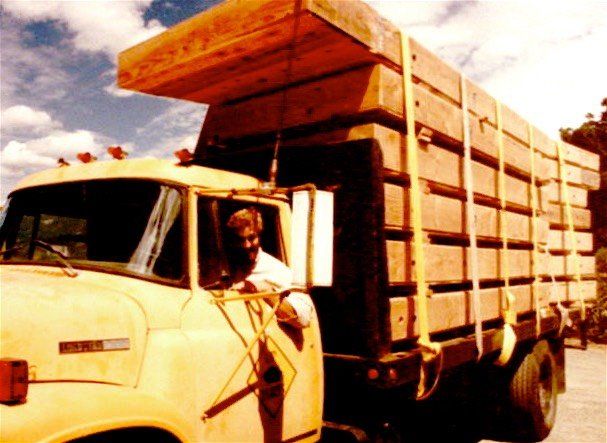 Yellow flatbed truck loaded with stacked wooden crates on a road under a bright sky