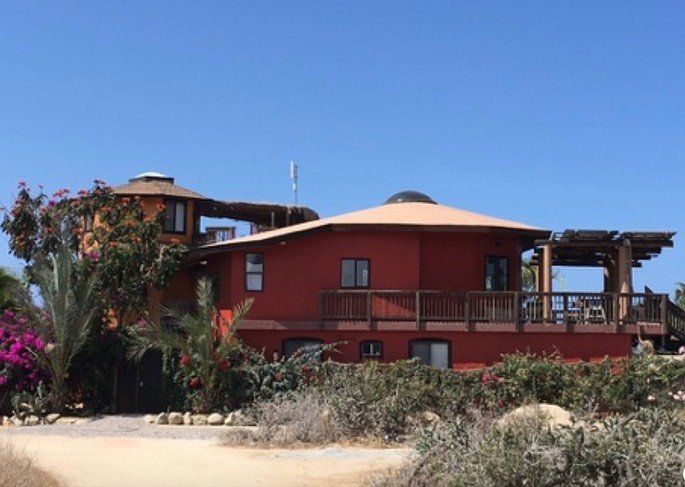 Red two-story house with balcony and trees under a clear blue sky