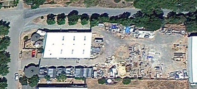 Aerial view of a construction site with a white-roofed building, parked vehicles, and dirt lots.