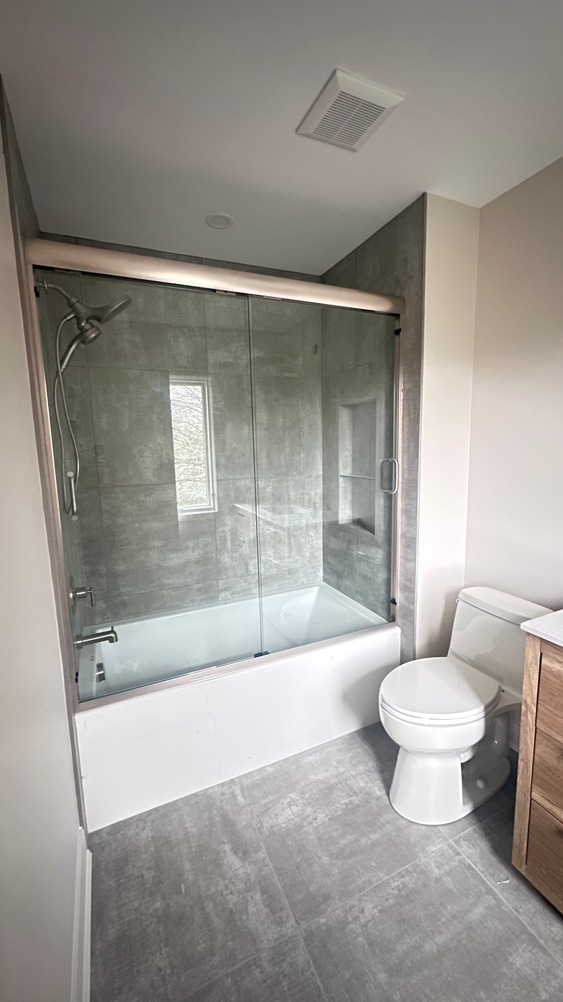 Grey tiles shower with glass as a separator alongside a white toilet.