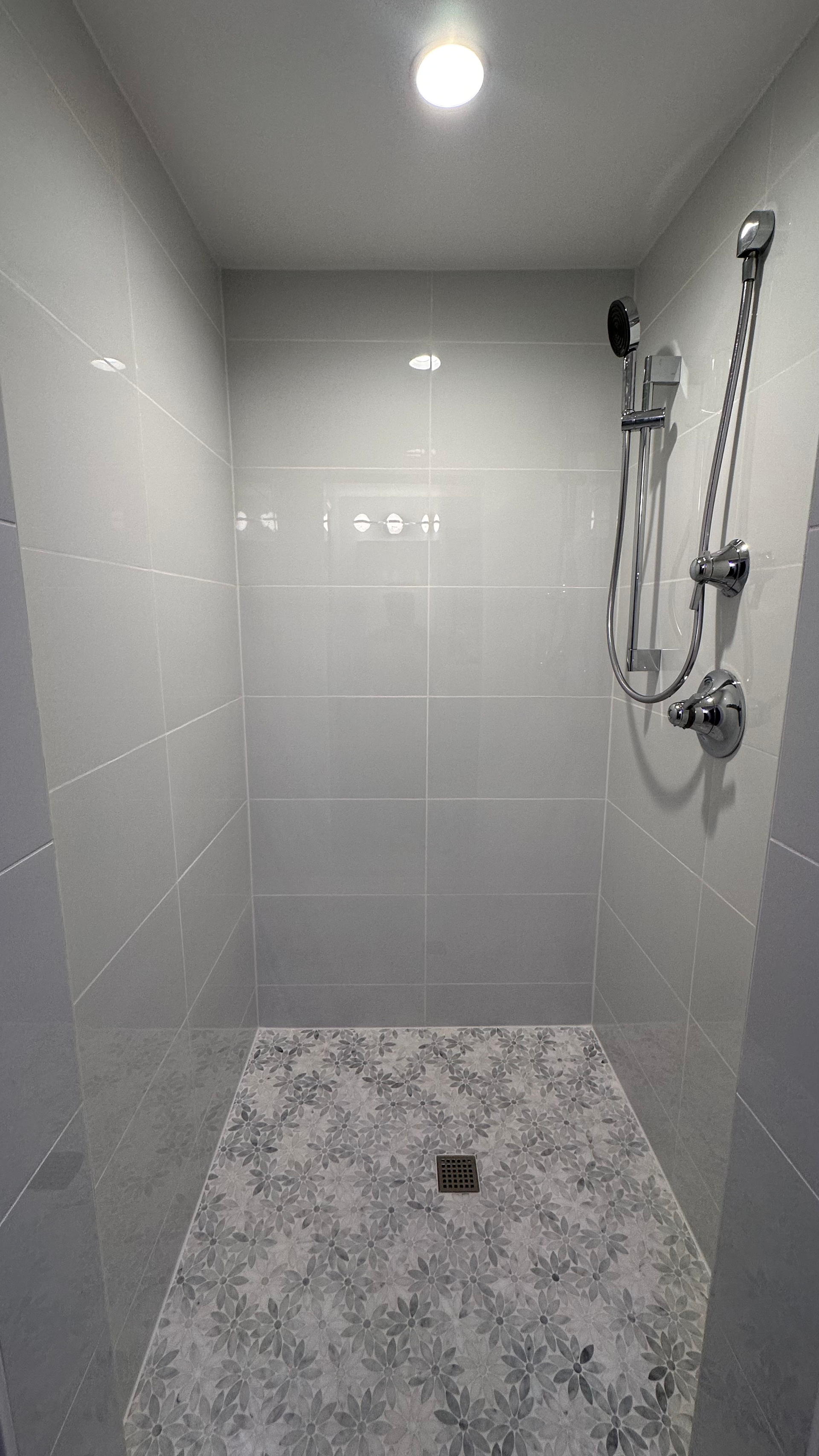 An off-white shower room with flower-textured tiles on the flooring.
