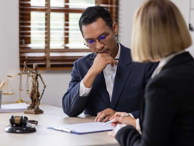 Two people in a law office reviewing documents at a desk, with scales of justice nearby.