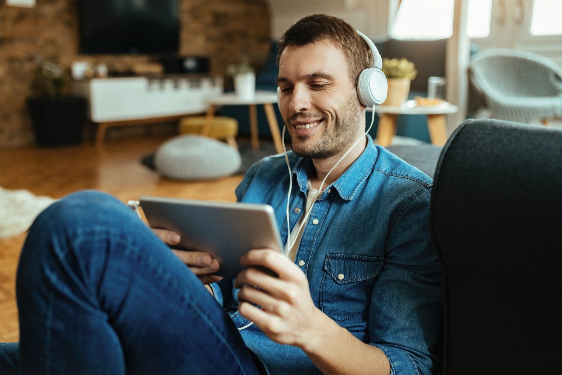 Hombre feliz relajándose en casa mientras usa el panel táctil y escucha música con auriculares Hombre feliz relajándose en casa mientras usa el panel táctil y escucha música con auriculares