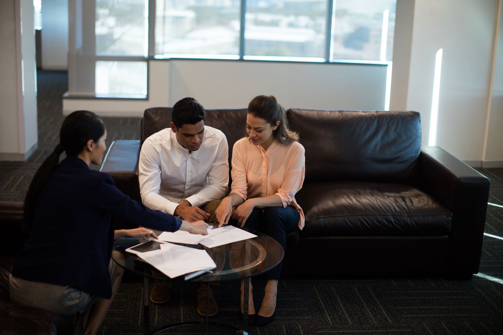 Three people reviewing documents around a coffee table in a bright office lounge.