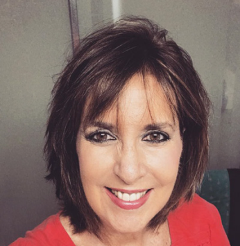Smiling woman with short dark hair and red top, facing the camera indoors