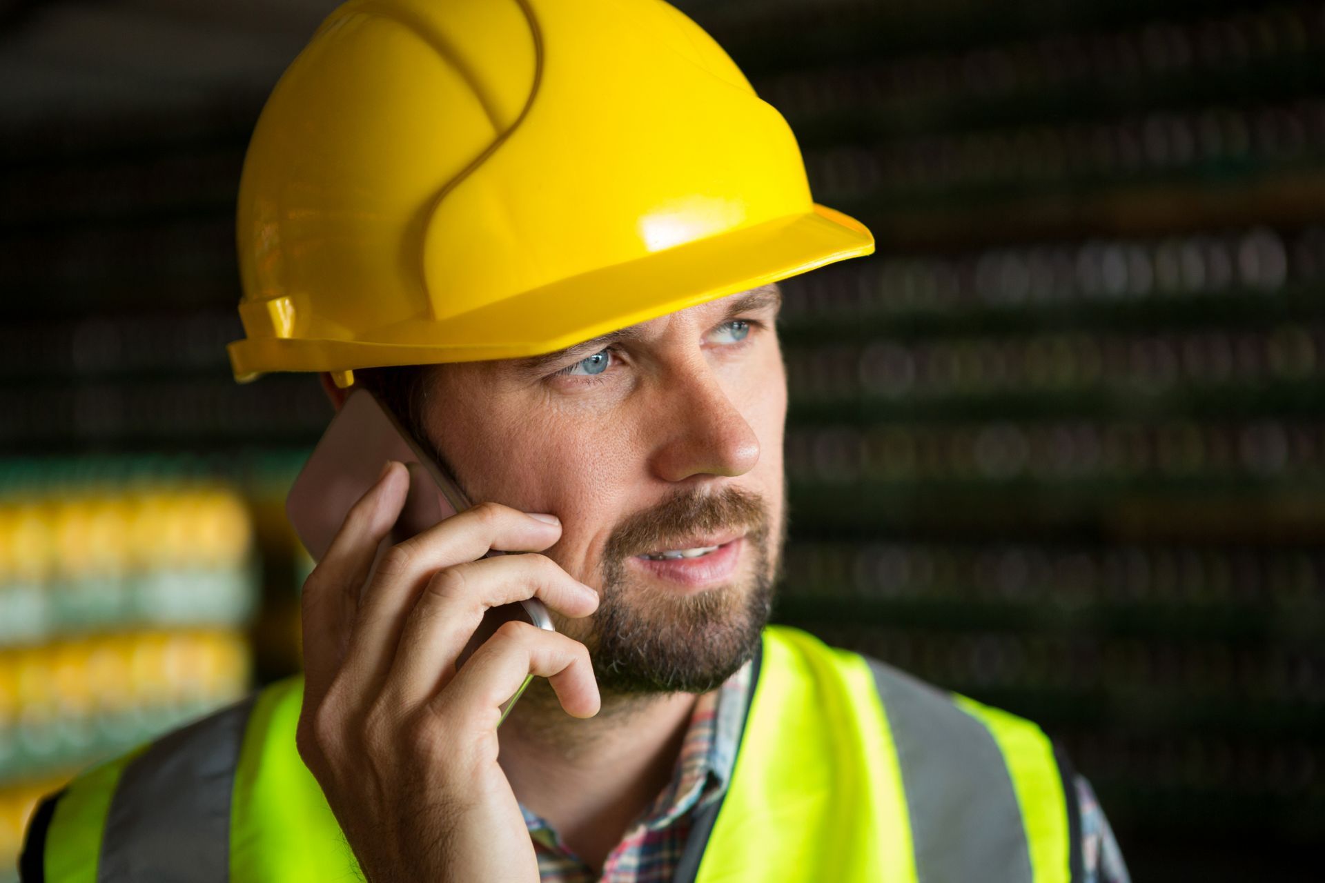 Worker in a yellow hard hat and safety vest speaking on a phone.