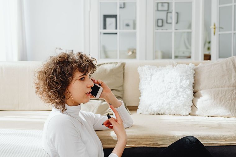 Person sitting on a couch, holding a phone to their ear in a bright living room