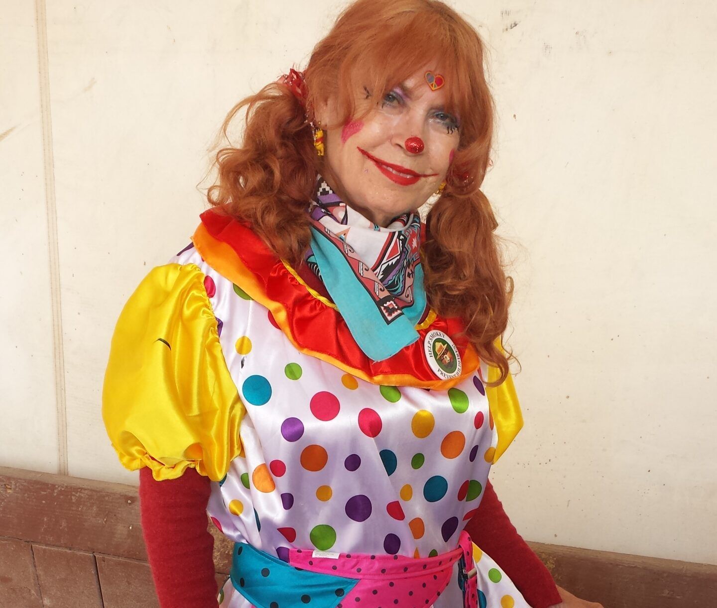 A woman in a clown costume is smiling for the camera