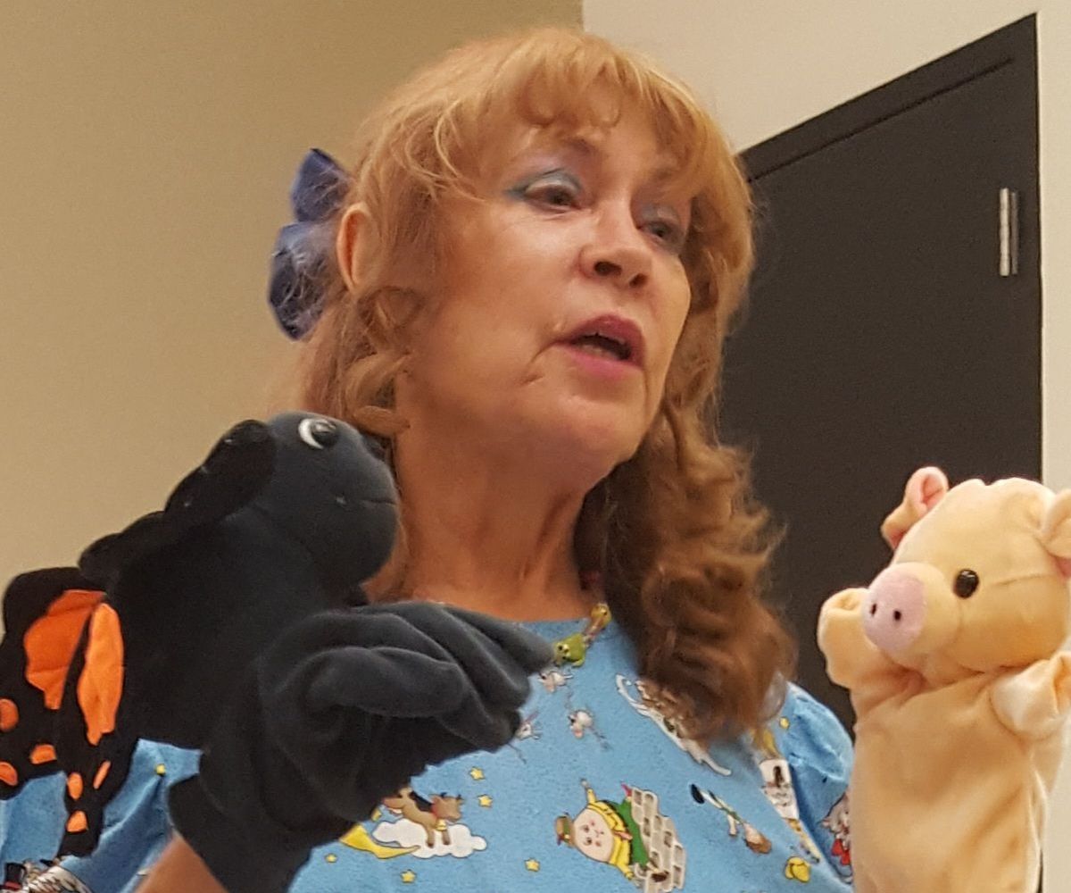 A woman is holding a puppet of a butterfly and a puppet of a pig