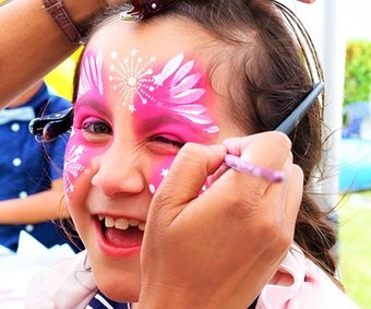A little girl has her face painted pink with a flower design