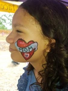 A little girl has a heart painted on her face that says mom.
