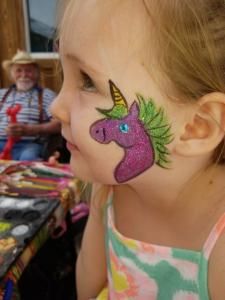 A little girl has a unicorn painted on her face.