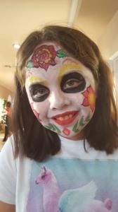 A little girl with her face painted and a unicorn shirt on.