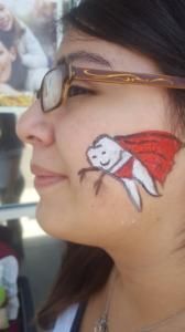 A woman with a tooth in a cape painted on her face.