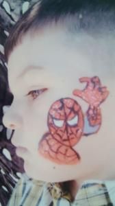 A young boy has a spiderman face painted on his face.