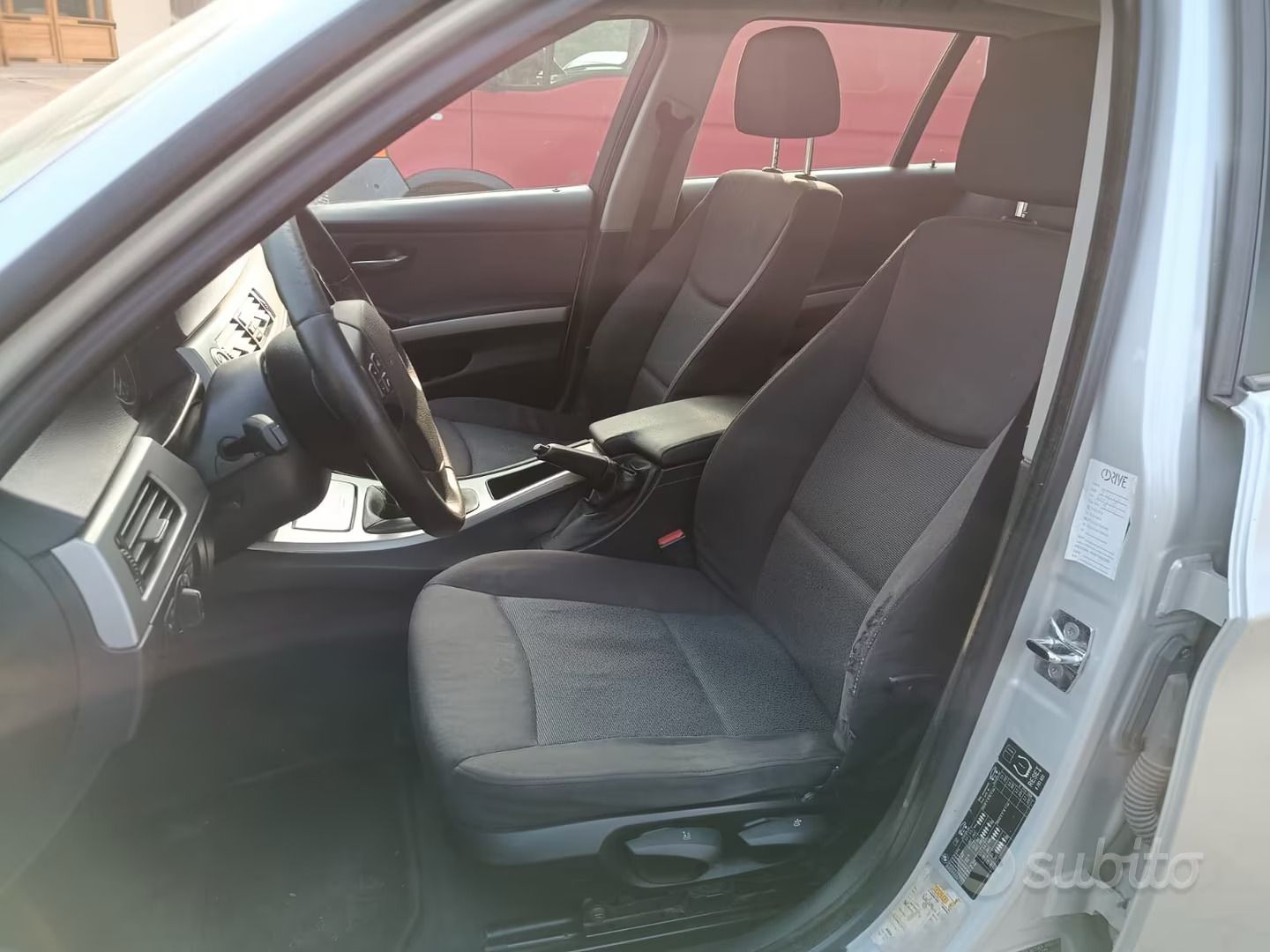 Interno dell'auto con sedili e console centrale neri, visto attraverso la portiera del conducente aperta.