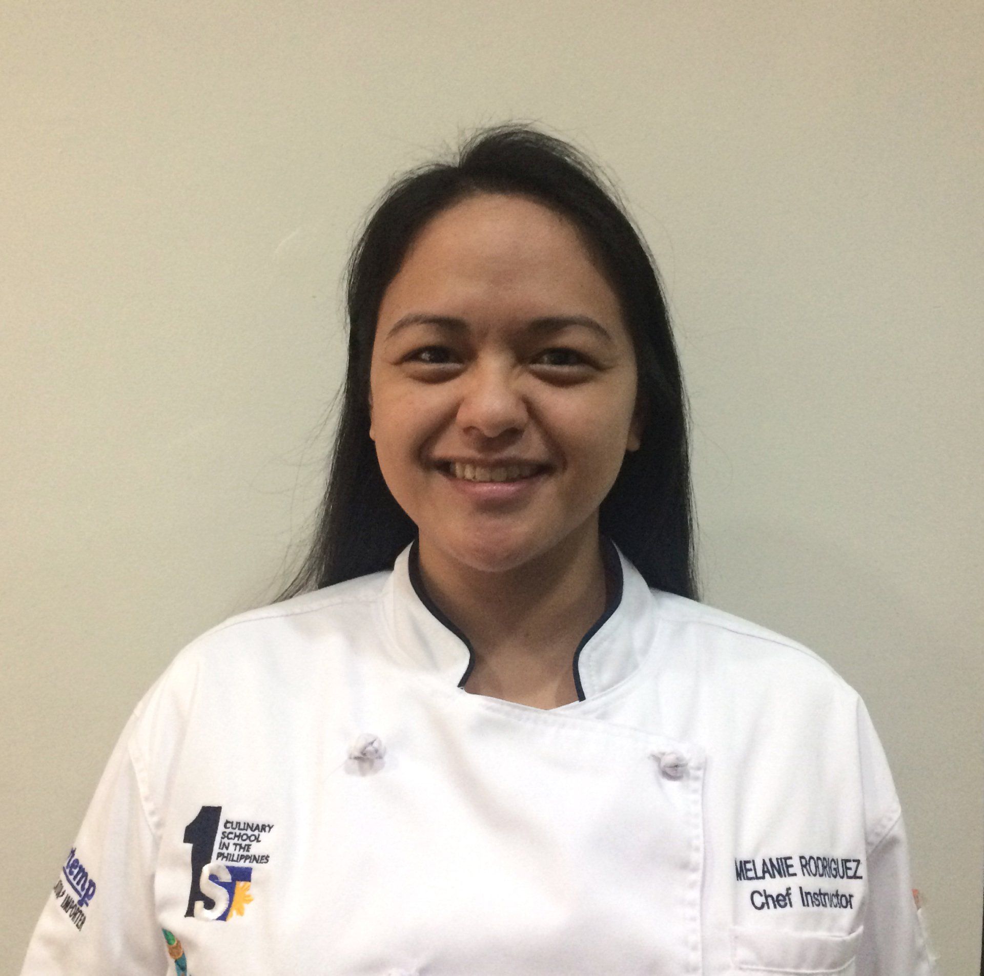 Smiling person in a white chef coat against a plain wall