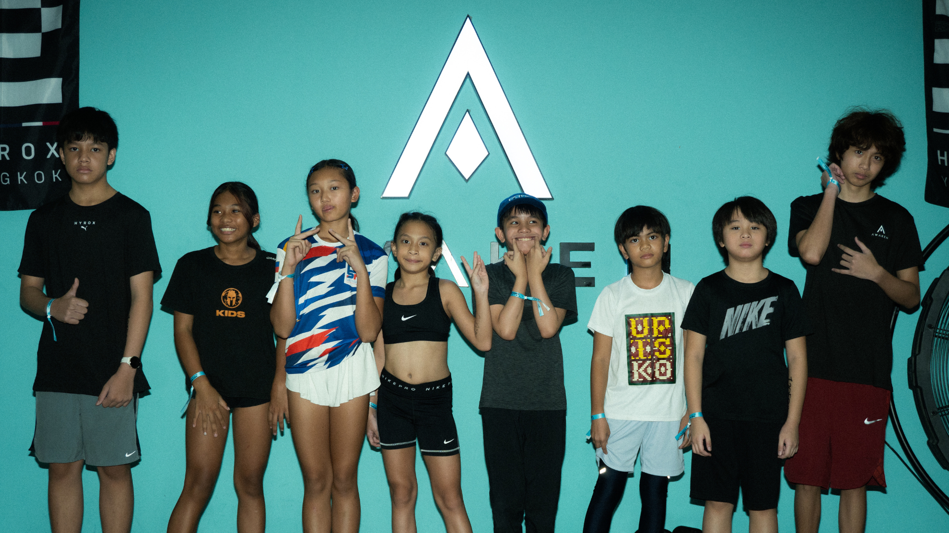 Group of children posing onstage in front of a teal backdrop with a white logo.