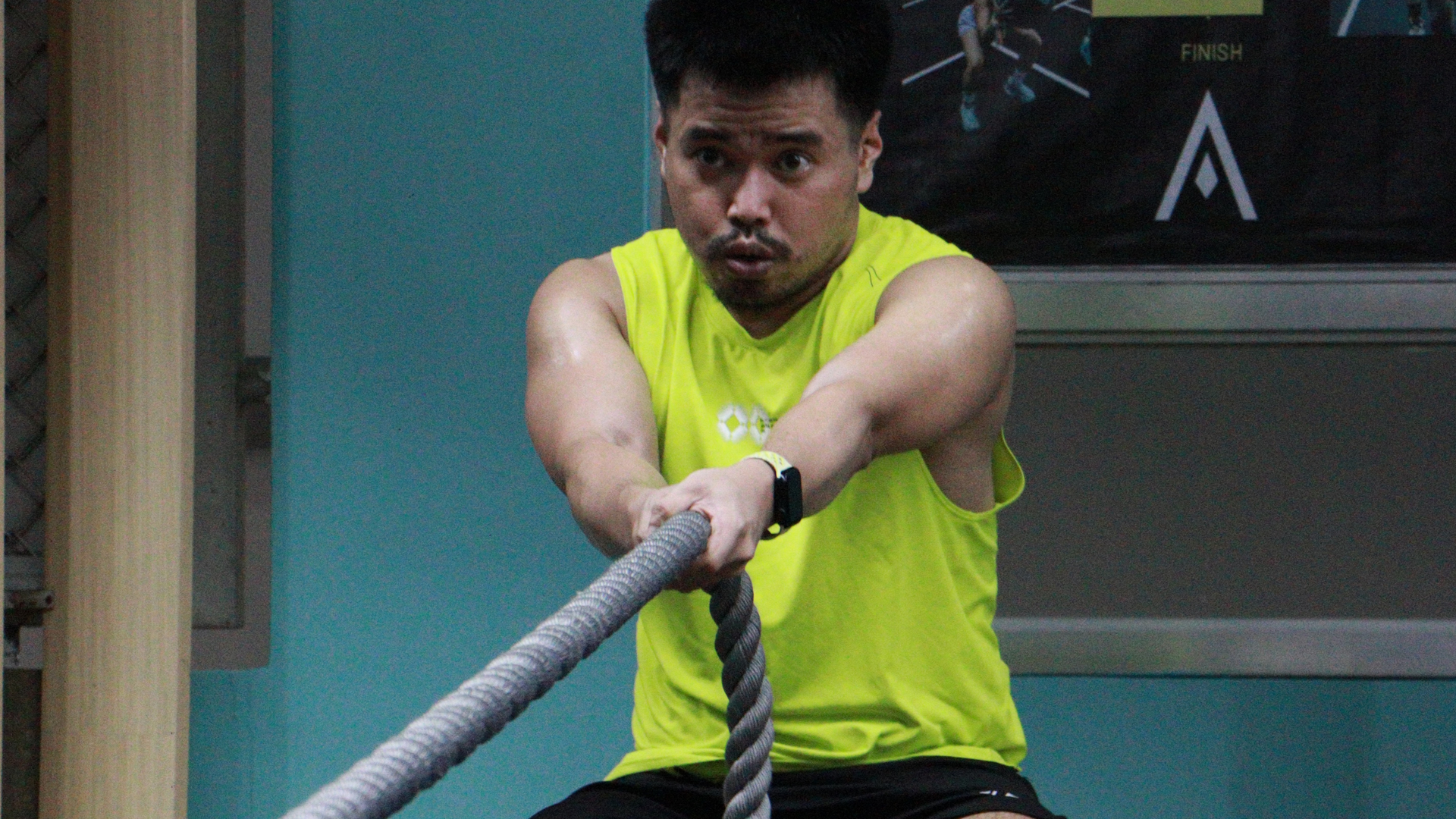 Person in a neon yellow shirt pulling a thick rope in a gym.