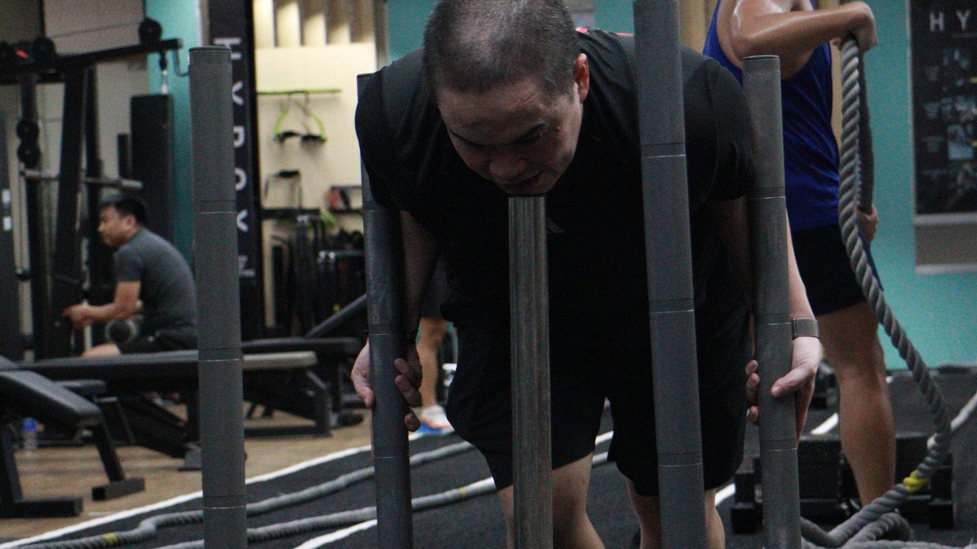 Man pushing a sled in a gym, leaning forward with effort beside a training lane