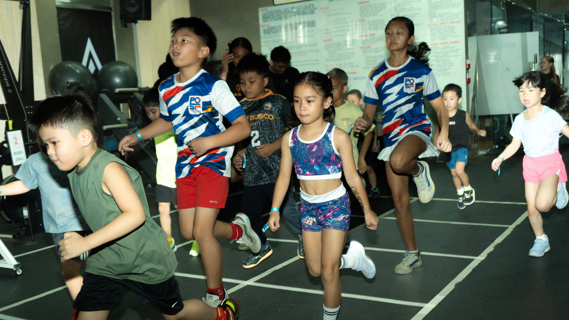 Children running in a relay race on an indoor track, wearing colorful athletic outfits.