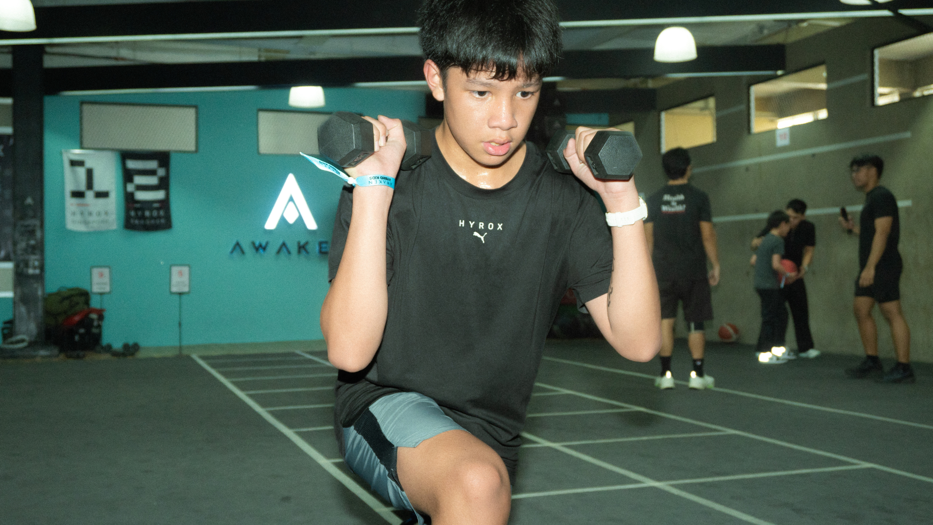 Person doing a dumbbell lunge in a gym with other exercisers in the background