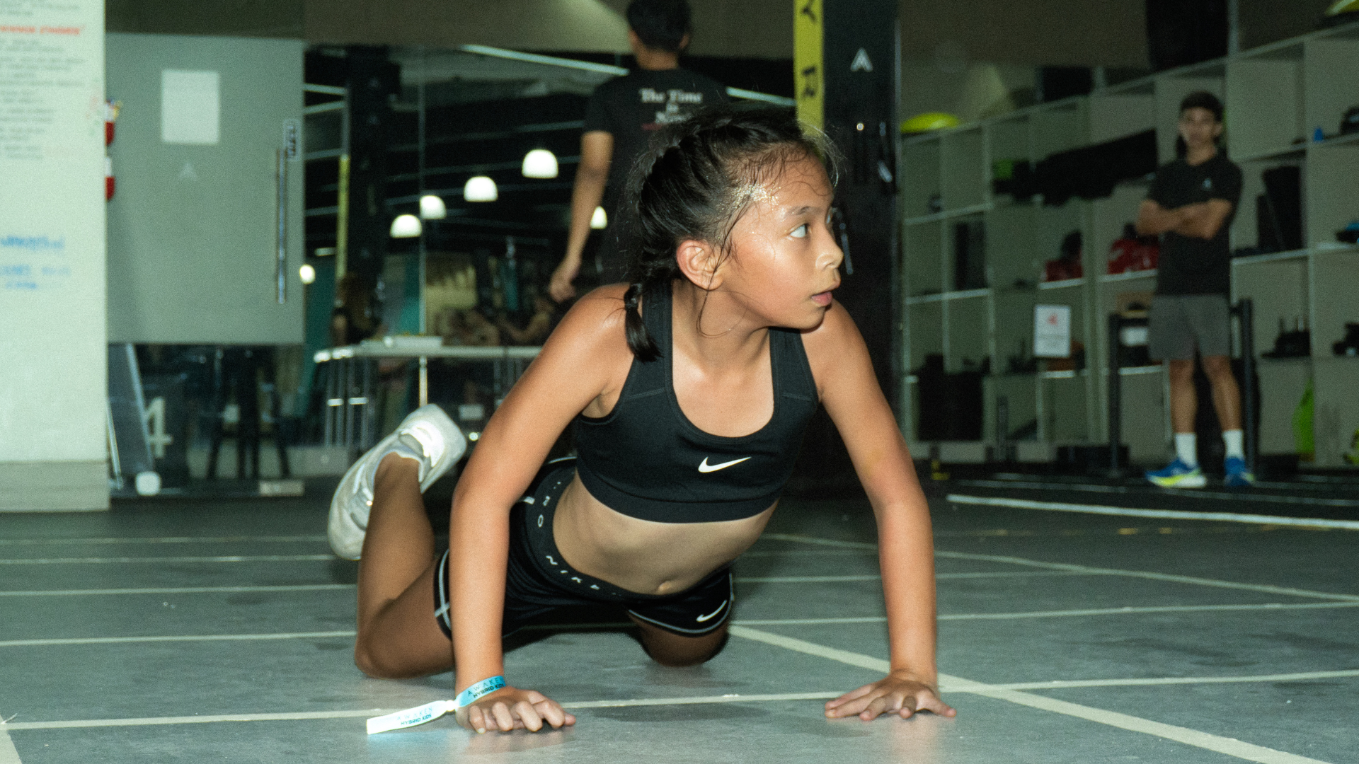 Athlete in black sportswear doing a floor push-up in an indoor gym lane.