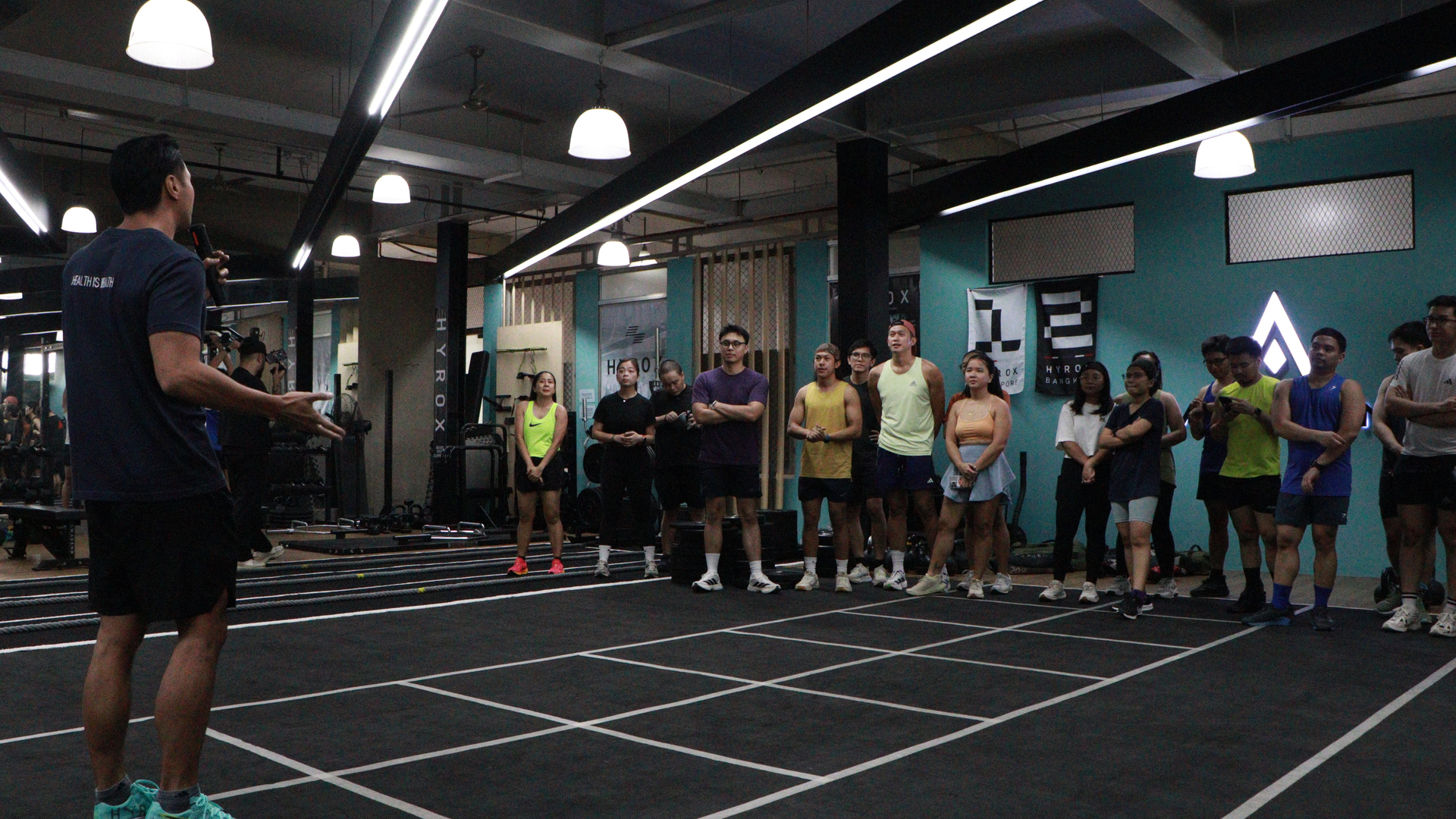 People standing in a gym facing a trainer during a group workout session