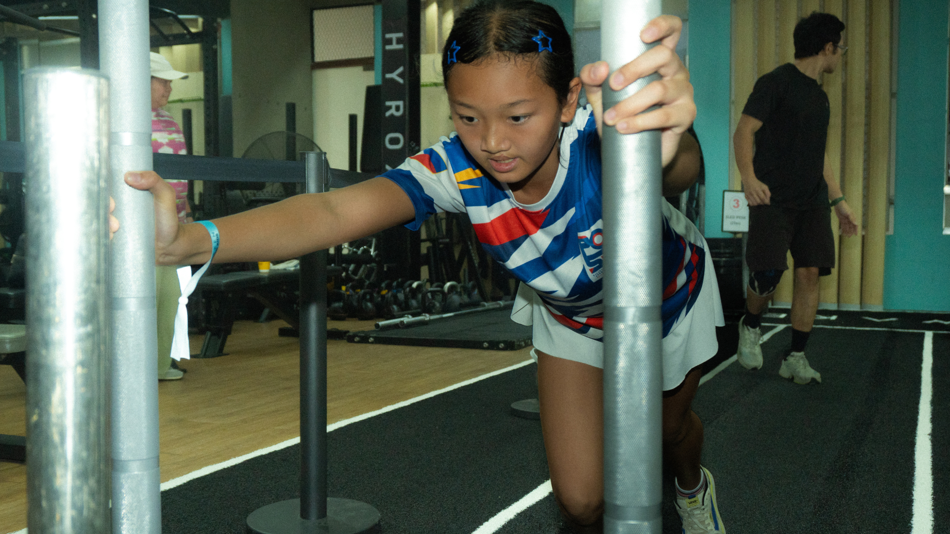 Child exercising between parallel bars in a gym, wearing a striped shirt and shorts.