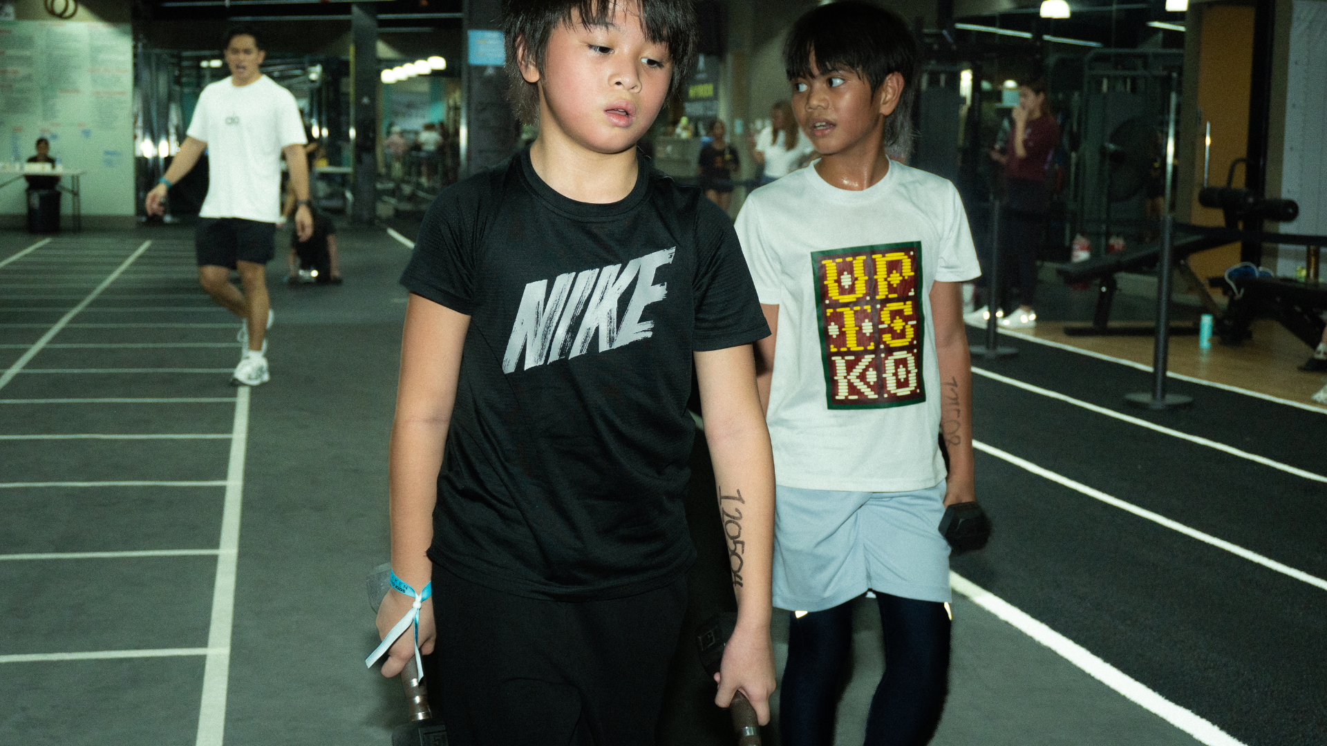 Two people walking on an indoor running track, one in a black Nike shirt and one in a gray shirt.