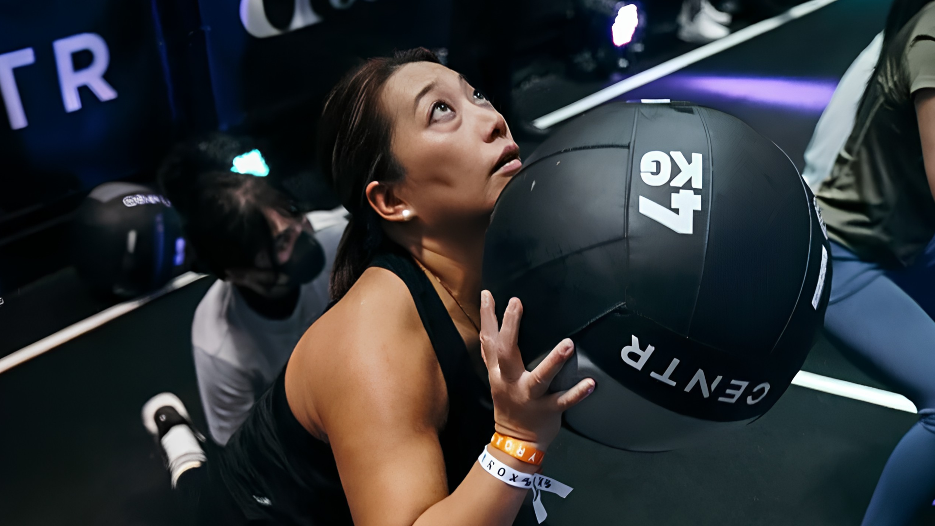 Woman doing wallballs in a HYROX competition, wearing black workout clothes.